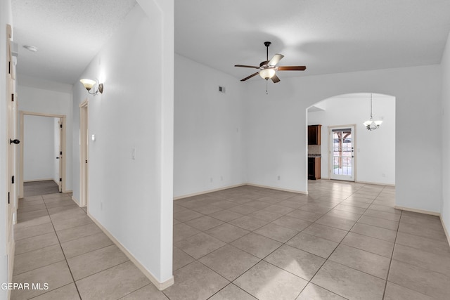 empty room with light tile patterned floors, baseboards, visible vents, arched walkways, and ceiling fan with notable chandelier