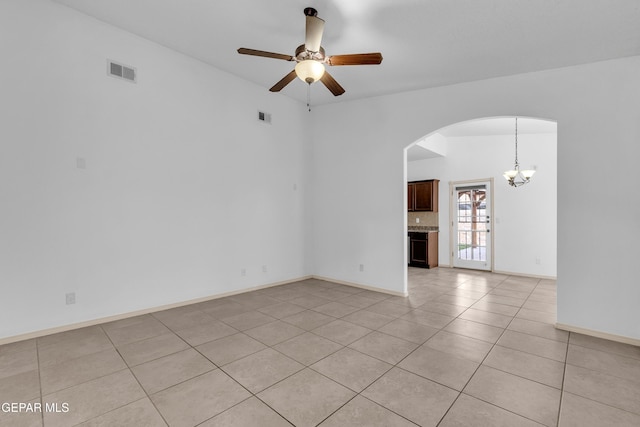 empty room with light tile patterned floors, ceiling fan with notable chandelier, visible vents, and arched walkways