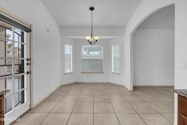 unfurnished dining area featuring light tile patterned floors, baseboards, arched walkways, and a chandelier