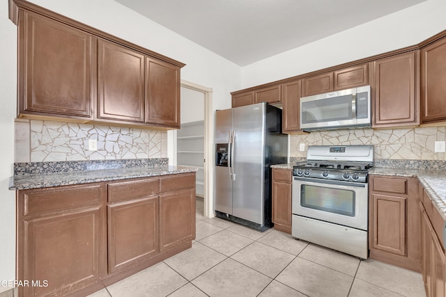 kitchen with light tile patterned floors, decorative backsplash, appliances with stainless steel finishes, and light stone countertops