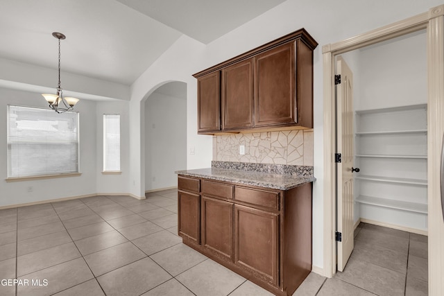 kitchen with light stone counters, backsplash, arched walkways, light tile patterned floors, and a chandelier