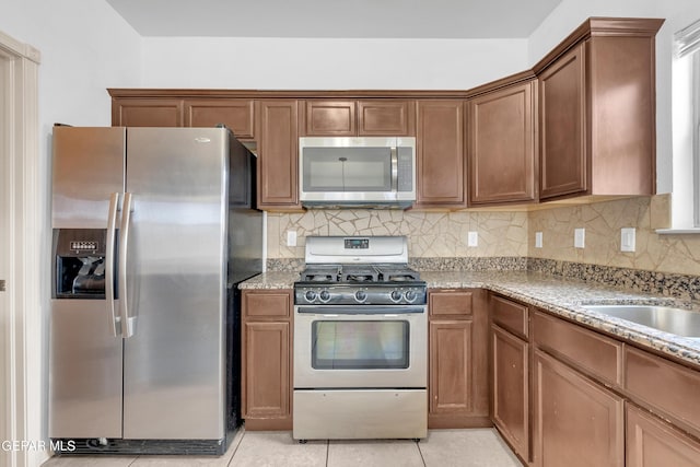 kitchen featuring backsplash, light stone countertops, light tile patterned floors, appliances with stainless steel finishes, and brown cabinetry