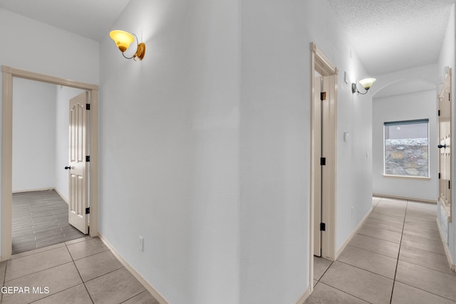 hall with light tile patterned flooring, arched walkways, a textured ceiling, and baseboards