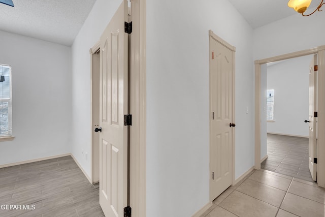 corridor featuring baseboards, light wood finished floors, and a textured ceiling