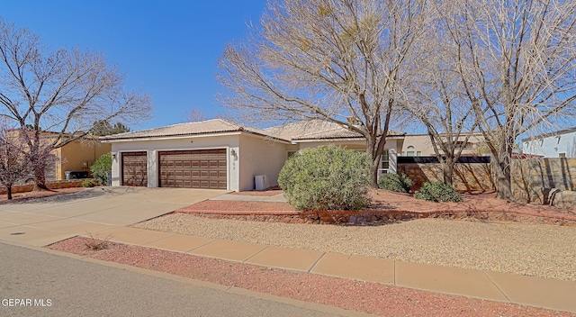 view of front of home featuring an attached garage, fence, a tile roof, stucco siding, and driveway