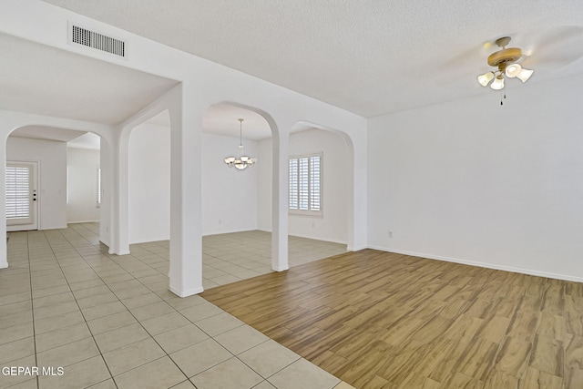 empty room featuring visible vents, light wood-style flooring, ceiling fan with notable chandelier, a textured ceiling, and arched walkways