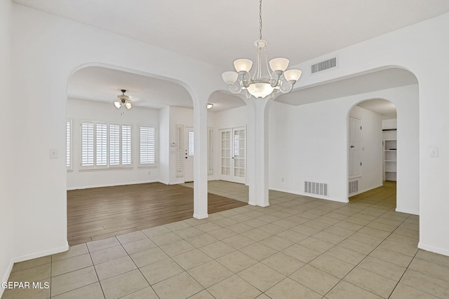 empty room featuring light tile patterned floors, visible vents, arched walkways, and an inviting chandelier