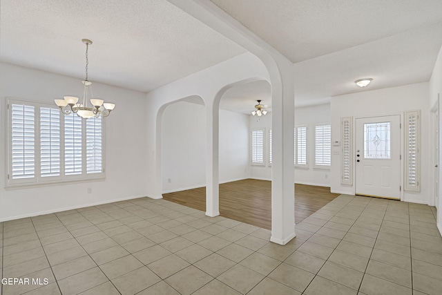 entrance foyer with an inviting chandelier, light tile patterned flooring, baseboards, and arched walkways