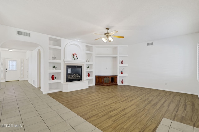 unfurnished living room with arched walkways, visible vents, a ceiling fan, and built in features