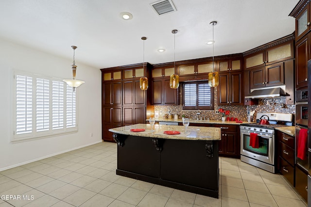 kitchen featuring visible vents, stainless steel gas range, hanging light fixtures, under cabinet range hood, and tasteful backsplash