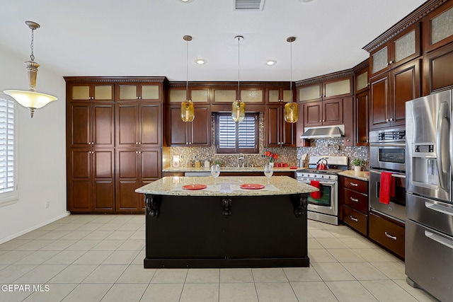 kitchen featuring under cabinet range hood, a kitchen island, tasteful backsplash, stainless steel appliances, and light tile patterned floors