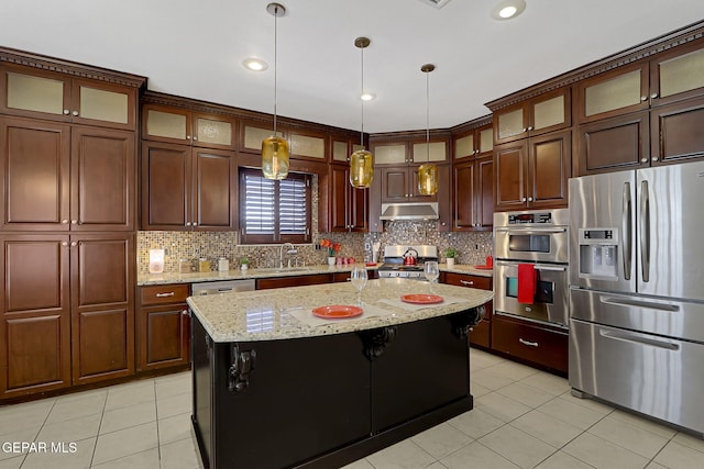 kitchen with light tile patterned floors, hanging light fixtures, under cabinet range hood, appliances with stainless steel finishes, and tasteful backsplash