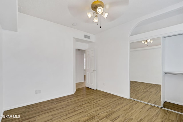 unfurnished room with wood finished floors, a ceiling fan, visible vents, and baseboards