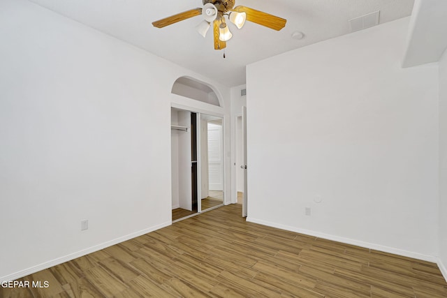 unfurnished bedroom with baseboards, light wood-type flooring, a closet, arched walkways, and a ceiling fan