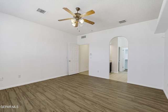 empty room featuring visible vents, arched walkways, light wood-style floors, and ceiling fan