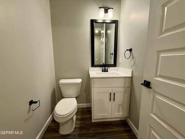 bathroom featuring baseboards, toilet, wood finished floors, and vanity