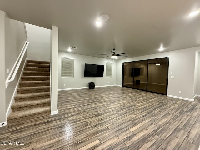 unfurnished living room featuring baseboards, wood finished floors, ceiling fan, and stairs