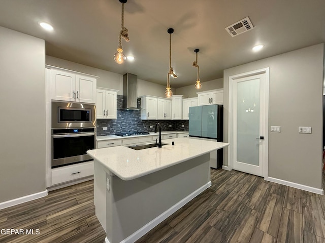 kitchen with visible vents, a sink, tasteful backsplash, stainless steel appliances, and wall chimney range hood