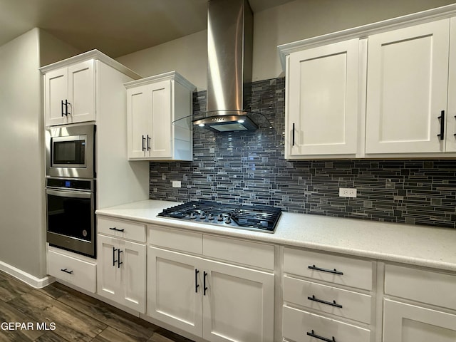 kitchen with light countertops, decorative backsplash, appliances with stainless steel finishes, white cabinetry, and wall chimney exhaust hood