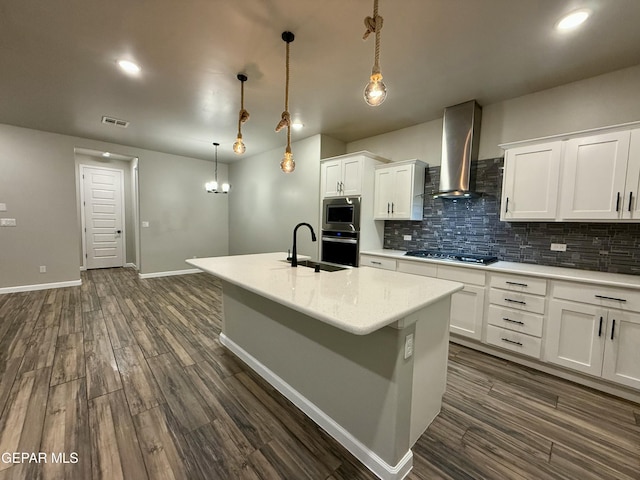 kitchen featuring visible vents, a sink, appliances with stainless steel finishes, wall chimney exhaust hood, and decorative backsplash