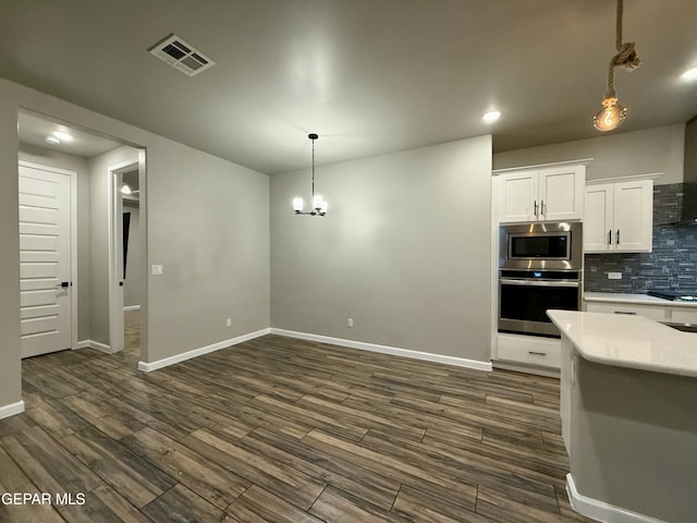 kitchen with dark wood finished floors, stainless steel appliances, decorative backsplash, white cabinets, and decorative light fixtures