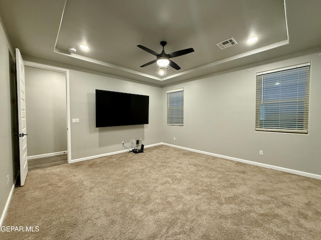 carpeted home theater with a tray ceiling, a ceiling fan, visible vents, and baseboards