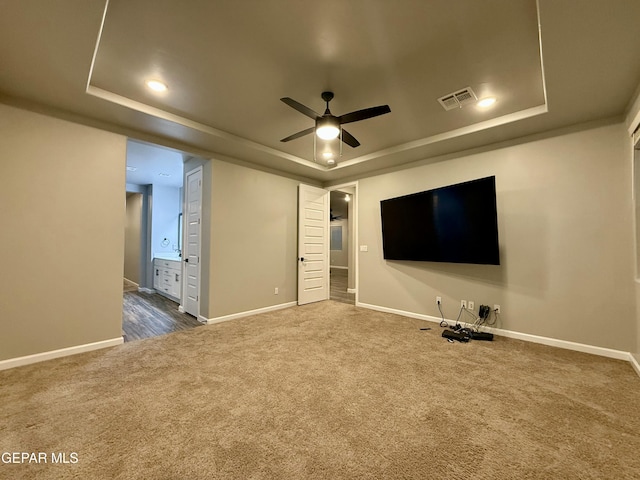 interior space with visible vents, baseboards, dark carpet, a tray ceiling, and a ceiling fan