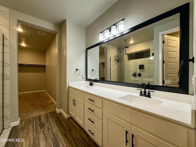 full bath with a sink, tiled shower, wood finished floors, and double vanity