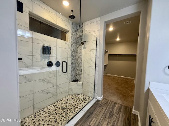 full bath featuring wood finished floors, a walk in closet, baseboards, and a stall shower