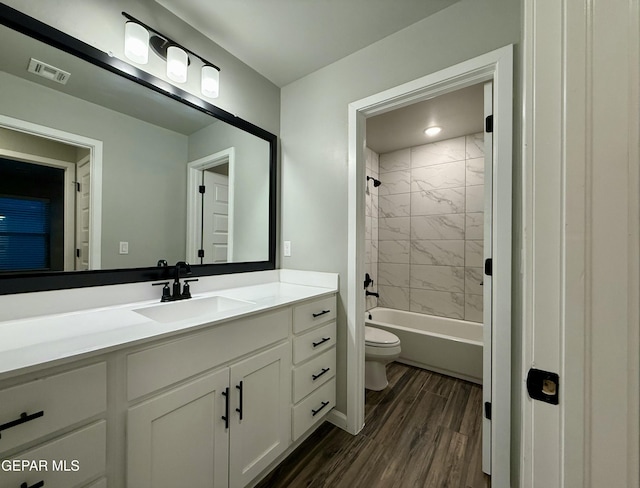 bathroom with visible vents, toilet, wood finished floors, vanity, and  shower combination