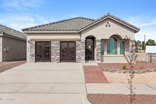 view of front facade featuring a tiled roof, stucco siding, driveway, stone siding, and an attached garage