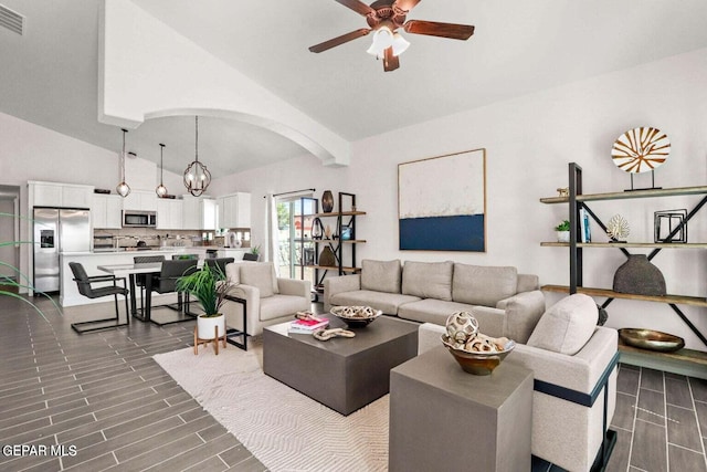 living room with arched walkways, ceiling fan with notable chandelier, wood tiled floor, and vaulted ceiling