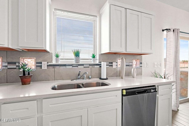 kitchen featuring stainless steel dishwasher, white cabinetry, backsplash, and a sink