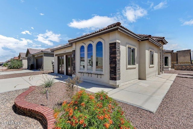 view of side of property featuring a tile roof, stone siding, and stucco siding