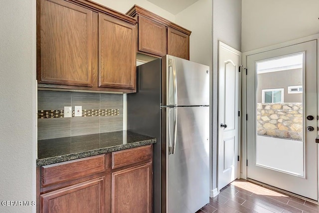 kitchen featuring backsplash, dark wood finished floors, dark stone countertops, freestanding refrigerator, and brown cabinetry