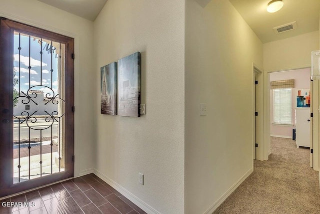 foyer featuring visible vents, baseboards, and dark colored carpet