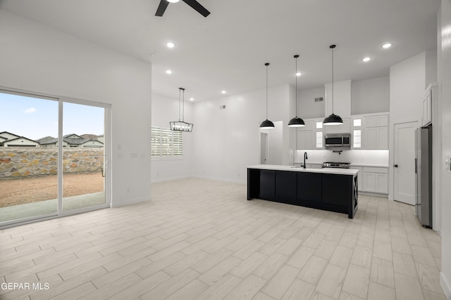 kitchen featuring a center island with sink, a high ceiling, stainless steel appliances, light countertops, and ceiling fan with notable chandelier