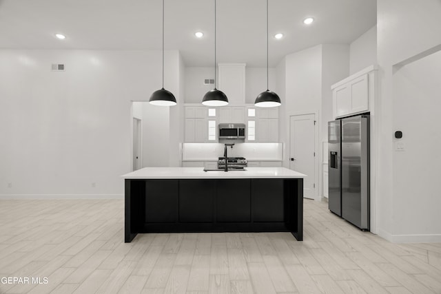 kitchen featuring an island with sink, a sink, light countertops, white cabinets, and appliances with stainless steel finishes