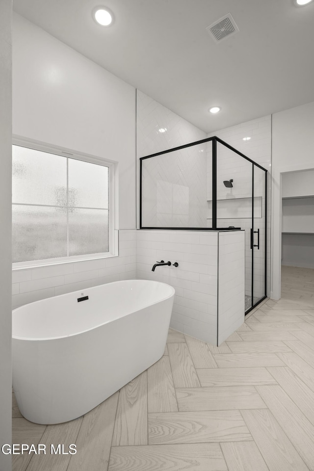 bathroom featuring visible vents, recessed lighting, a stall shower, a freestanding bath, and tile walls