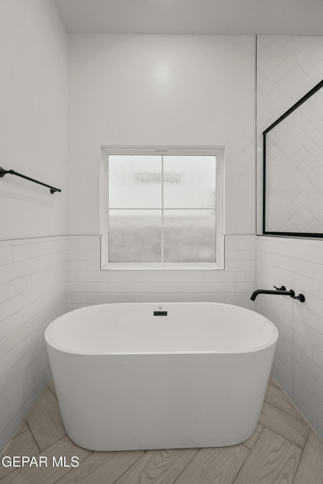 bathroom with a soaking tub, tile walls, and wainscoting