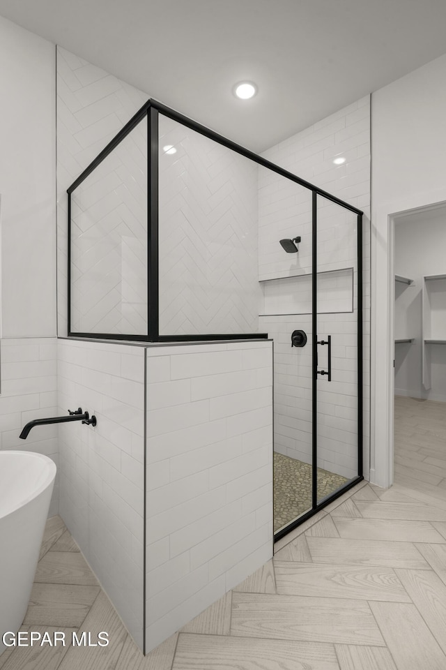 full bathroom with recessed lighting, a stall shower, a freestanding bath, a spacious closet, and tile walls