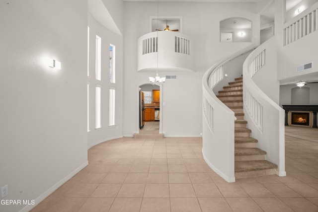 tiled entryway featuring visible vents, a warm lit fireplace, a high ceiling, baseboards, and stairs