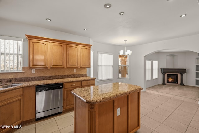 kitchen with a kitchen island, dishwasher, light stone counters, light tile patterned flooring, and a glass covered fireplace