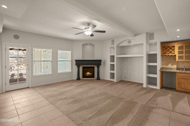 unfurnished living room with built in features, light colored carpet, a lit fireplace, wet bar, and a textured ceiling