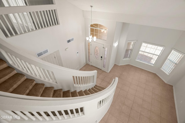 tiled entrance foyer featuring stairs, an inviting chandelier, visible vents, and high vaulted ceiling