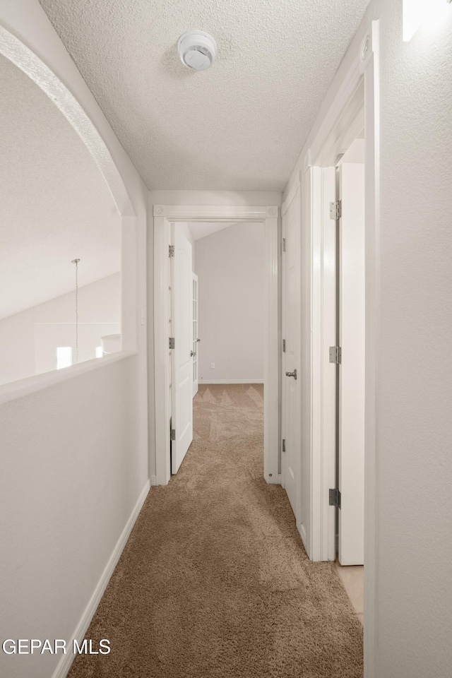 corridor with baseboards, arched walkways, carpet floors, and a textured ceiling