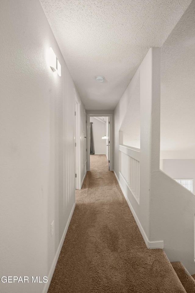 hall with baseboards, a textured ceiling, and carpet