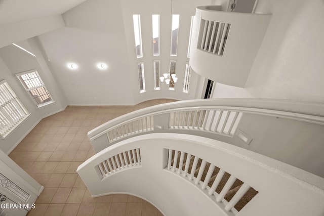 staircase featuring tile patterned floors, a notable chandelier, baseboards, and a towering ceiling