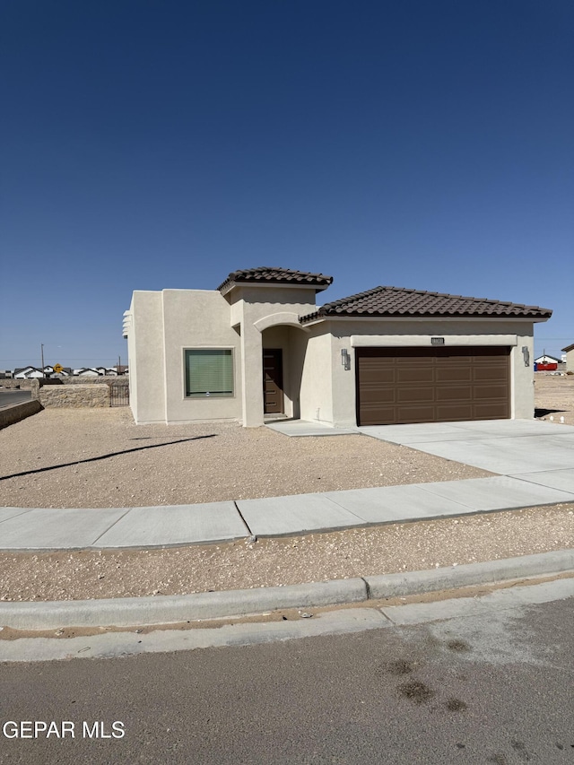 view of front of house with stucco siding, a tiled roof, an attached garage, and driveway