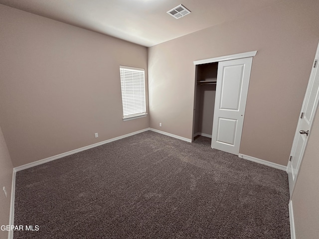 unfurnished bedroom with a closet, visible vents, baseboards, and dark colored carpet